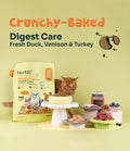 Cat beside Notti Crunchy-Baked Digest Care pouch with raw duck, venison, turkey and fresh ingredients displayed on stands